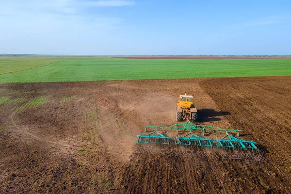 Tractor drives through the field cleaning dried grass and plowing, seasonal harvesting on countryside, drone shooting from height. Equipment and machines for agricultural industry
