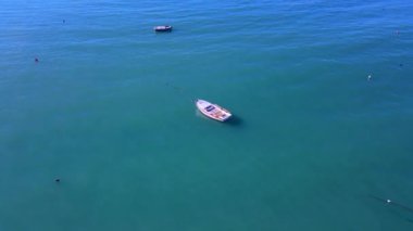 Turkuaz dalgalı deniz suyunda küçük beyaz bir yelkenli.