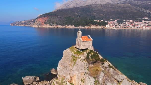 Historical stone chapel with red roof on small rocky island — Wideo stockowe