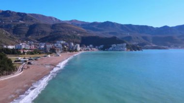 Kameralı insansız hava aracı, Avrupa 'nın Budva kentindeki sahil şeridi boyunca uçuyor, insanların yürüdüğü, dağlarla çevrili, güneşli bir günde