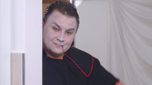 Junger Mann mit Make-up und schwarzem Vampirkostüm guckt um die Ecke und gestikuliert, um sich zu beeilen. Freunde kommen zu spät zur Halloween-Party — Stockvideo