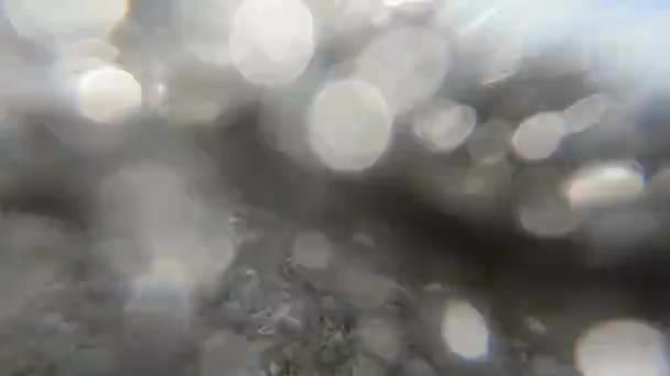 Lichte schuimgolven bedekken camera 's op zandstrand, kleine brokstukken en kiezelsteentjes van bodem tuimelen onder het water, schieten vanuit lage hoek. Prachtige zonnige dag aan zee — Stockvideo