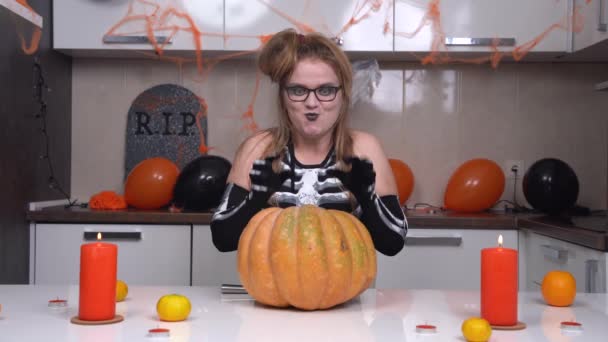 Blodtörstig ung kvinna i Halloween skelett kostym skrattar ondskefullt och lömskt stroke pumpa, sticker kniv i den. Förbered dig för lömsk temafest — Stockvideo