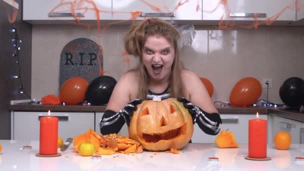 Młoda blondynka w kostiumie szkieletowym ze strasznym grymasem na twarzy przywołuje nad latarnią, śmieje się złowieszczo i zdmuchuje świeczkę w Halloween — Wideo stockowe