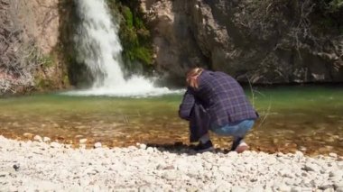 Turist, dağ ormanlarında yürürken aşağıdan şelalenin fotoğraflarını çekiyor, cep telefonu kullanıyor, arkadan görüyor. Genç bayan blogcu seyahat vlog 'u için içerik oluşturuyor