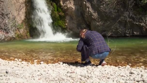 Turista fotí vodopád z nízkého úhlu při chůzi v horském lese, pomocí mobilního telefonu, pohled zezadu. Mladá žena blogger dělá obsah pro její cestování vlog — Stock video