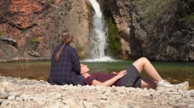 Beyaz şelale ve göle karşı genç bir kadın ve kız arkadaş