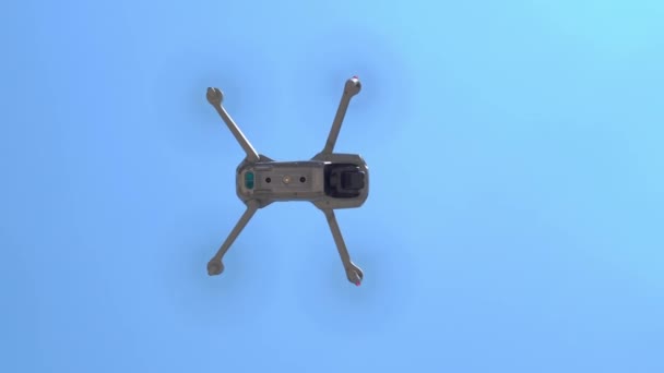 Drone moderno com uma câmera e hélices de trabalho pairando no ar acima do solo durante a vigilância, painel inferior do gadget, vista de baixo para cima — Vídeo de Stock