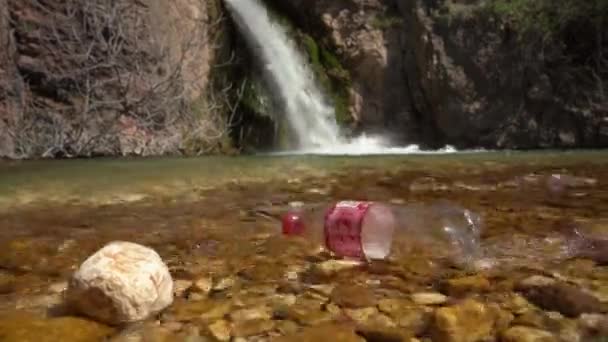 12. Juni 2021, Budva, Montenegro: Am Flussufer schwimmt eine Coca-Cola-Flasche aus Plastik, im Hintergrund rauscht ein Wasserfall aus nächster Nähe zwischen den Felsen. Umweltverschmutzung und Abfallrecycling — Stockvideo