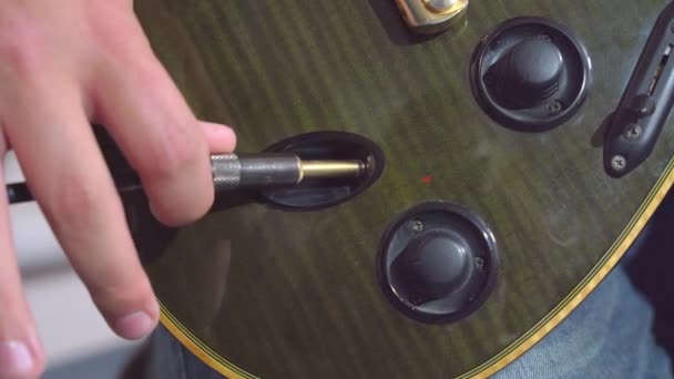 A személy bedugja a drótot egy elektromos gitár bemeneti emelőjébe, hogy elkezdjen hangszeren játszani, közelről. A hobbi és a szórakozás fogalma — Stock videók