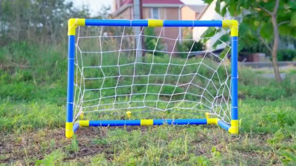 Футбольный мяч катится к пустым футбольным воротам для детей, вид спереди. Дети играют в футбол, и кто-то сделал слабый шаг, не забив гол. активный отдых — стоковое видео