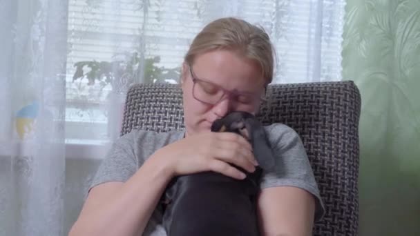 Sad young woman cuddles with cute dachshund puppy while sitting in rocking chair at home or in rehabilitation center. Mental health therapy with pets that help you cope with emotional problems — Vídeo de stock