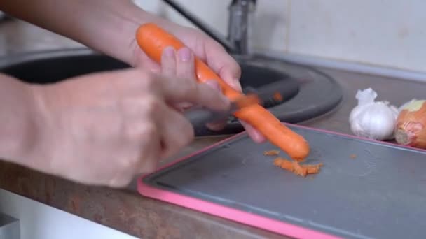Femeia tânără cojește morcovul deasupra plăcii de tăiere în bucătărie — Videoclip de stoc