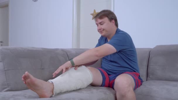 Young silly man incorrectly takes off cast from his leg without help of doctor. Pretender cheated that he had broken leg to get the insurance payout — Vídeo de stock