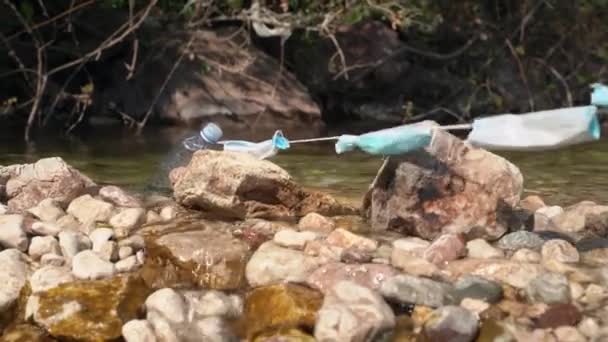 사용되고 부적절하게 처리 된 의료용 마스크의 신축성있는 밑줄에 걸린 플라스틱 병. 자원 봉사자가 청소하는 날 쓰레기 더미를 강에서 끌어올리고 있습니다. 환경 오염 — 비디오