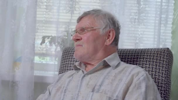 Uomo anziano con i capelli grigi in occhiali si siede sulla sedia a dondolo — Video Stock