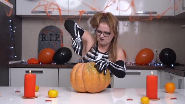 Woman in sinister skeleton costume is preparing to celebrate Halloween, carving top of pumpkin with stalk and core to make jack-o-lantern to decorate apartment for party — Stock Video