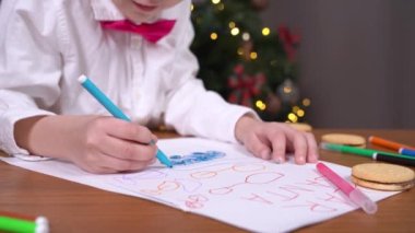 Çocuk yazmayı öğreniyor. İyi çocuk ailesi için tebrik kartı çekiyor. Çocuk Noel arifesinde Noel Baba 'ya bir dilek mektubu yazıyor. Arka planda bulanık bir Noel ağacı.