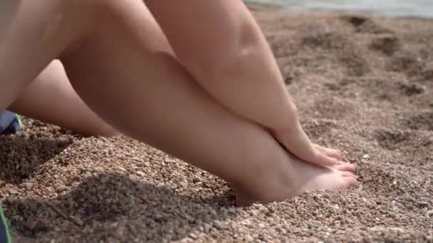 Mujer aplica protector solar en la pierna sentado en la playa de guijarros del mar — Vídeo de stock
