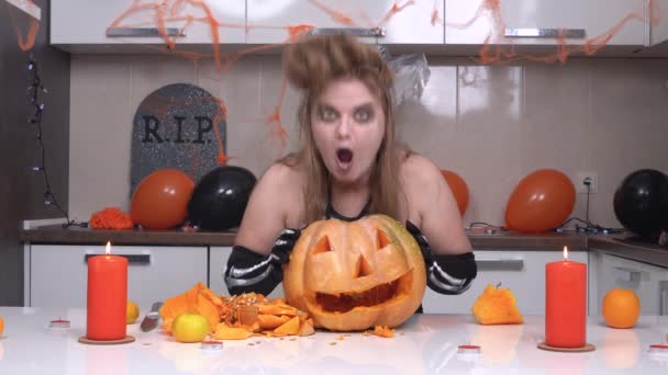 Blonde woman in festive outfit is preparing for spooky costume party in honor of Halloween and made jack-o-lantern. She looks inside pumpkin and sees something shocking — Stock Video