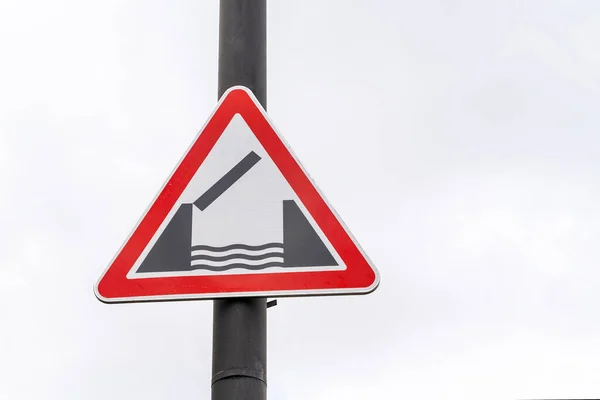 Drogowy znak ostrzegawczy mostu zwodzonego na biegunie na zewnątrz, szare i białe niebo burzy na tle, zbliżenie. Infrastruktura miejska. Symbole i znaki informacyjne — Zdjęcie stockowe