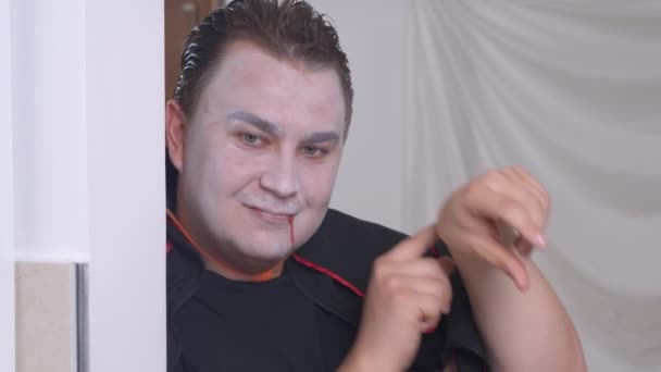 Jonge man in gemaskerde vampier kostuum en make-up, met imitatie van bloedsporen op het gezicht, raakt de arm horloge, proberen om iemand haastig en angstaanjagende grijnzen. Halloween concept — Stockvideo