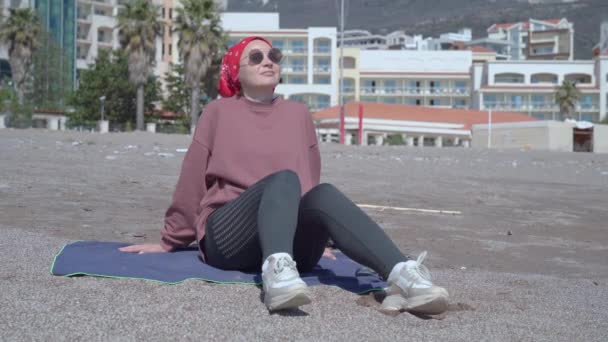 Señora con pañuelo rojo y gafas de sol se sienta en la arena de la playa de mar — Vídeos de Stock