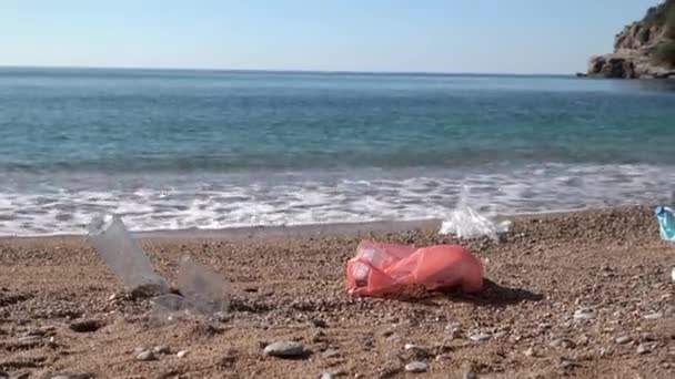 Sacos de plástico e garrafas na praia de areia perto de ondas rolantes — Vídeo de Stock