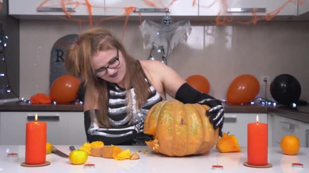Kvinna i läskig skelett kostym och med konstig frisyr snidade ansikte på pumpa och gjorde jack-o-lantern för Halloween fest. Hon är nöjd med resultatet och tittar på sin skapelse från alla håll — Stockvideo