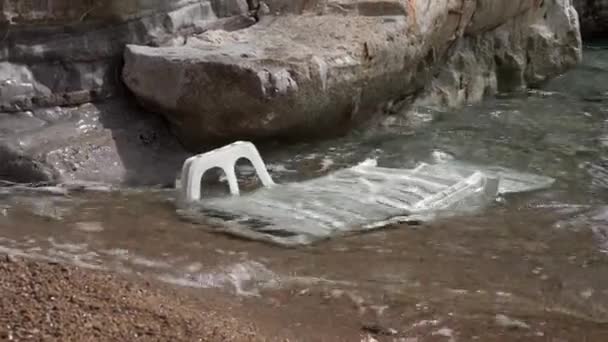 Sedia a sdraio galleggia in onde marine rotolando sulla spiaggia vicino a scogliere — Video Stock