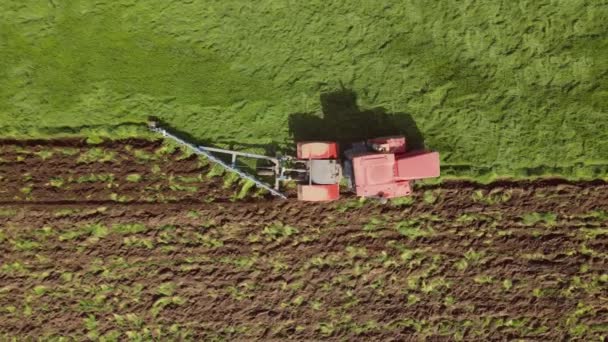Rode landbouwtrekker rijdt langs veld en ploegt grond — Stockvideo