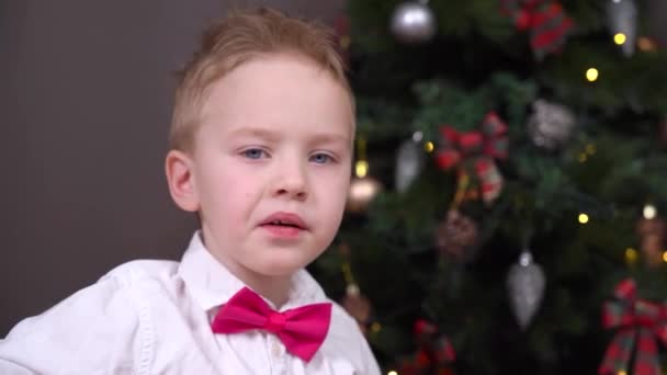 Retrato de niño travieso en camisa blanca con pajarita, comiendo dulces que se ha estado comportando mal todo el año por lo que no recibirá regalos de Santa para Navidad — Vídeos de Stock
