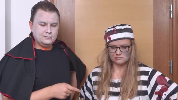 Young man in mantle of Count Dracula and blonde woman in striped prisoner murderer costume with cap make edifying gesture with their index finger to child or pet before leaving for Halloween party — ストック動画