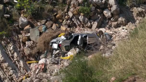 Car flew off serpentine road down the cliff, and now wreckage of crashed car lies on rocks after terrible accident, top view. Poorly equipped highways or drunk driving leads to bad result — Stock Video