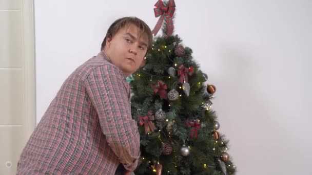 Zvědavý netrpělivý mladý muž je chycen při činu snaží najít a otevřít svůj nový rok dárek před dovolenou pod zdobené vánoční stromeček — Stock video