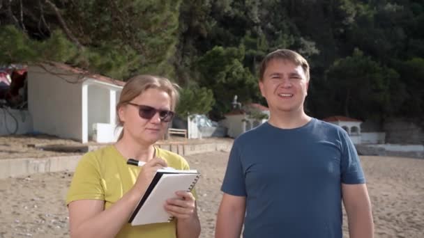 Man roept vriend in de buurt dame met het schrijven in notebook op het strand — Stockvideo