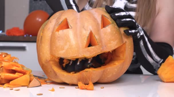 Person makes jack-o-lantern to decorate house for Halloween party, close up. Woman pulls entrails of pumpkin out with spoon, she puts hand through mouth hole and wiggles fingers — Stock Video