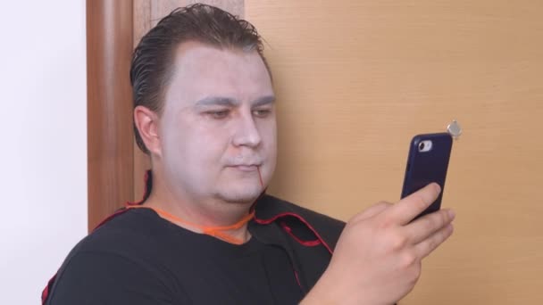 Bărbat tânăr în costum de vampir mascat și se machiază, imitând urme de sânge pe față, navigând în telefonul mobil, se uită la cineva și face degetul mare în sus. Conceptul de Halloween — Videoclip de stoc