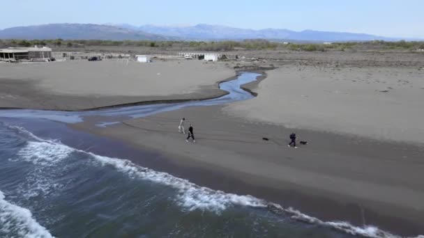 Turistas caminham ao longo da praia de areia molhada com edifícios distantes — Vídeo de Stock