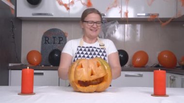 Önlüklü tatlı sarışın kadın Cadılar Bayramı partisi için balkabağı Jack-o-Lantern yaptı mumları üfledi ve masanın altına baktı. Daire tatil için dekore edilmiştir.
