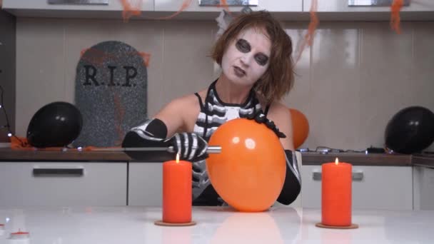 Frightening sorceress with creepy makeup in skeleton costume performs sinister ritual with sharp knife heated on fire of candles with which she pierces balloon. Show at Halloween party — Stock Video