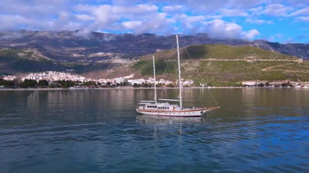 Large vintage sailboat is anchored in the middle of sea bay, illuminated by golden rays of sun. Beautiful seascape with calm water surface and mountains covered with forest — Stock Video