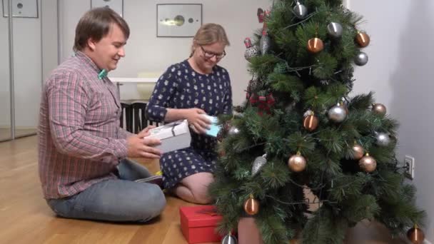 Веселая пара принимает подарки возле елки в номере — стоковое видео