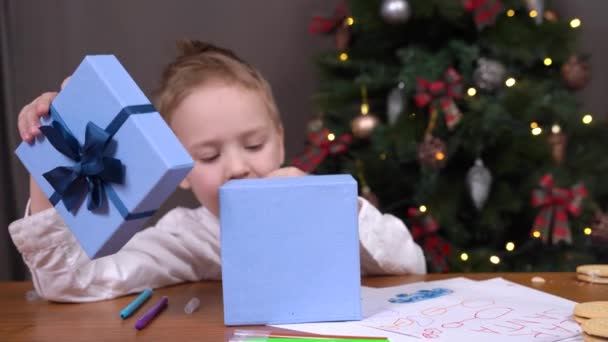 Милый мальчик с подарком Рождественская коробка ест сладости за столом — стоковое видео