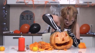 Tuhaf sarışın kadın Cadılar Bayramı feneri yapmak için balkabağından hamur topluyor, üzerinde yüz hatları kesilmiş bir çerçeve bırakıyor, sonra her şeyi tekrar birleştiriyor ve yeniden başlıyor.