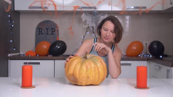 Kobieta wybrała najlepszą dynię na świąteczny stół i cieszy się z tego głaskania warzyw, całowania i przytulania. Dom jest ozdobiony świecami, balonami i fałszywym nagrobkiem na Halloween party — Wideo stockowe