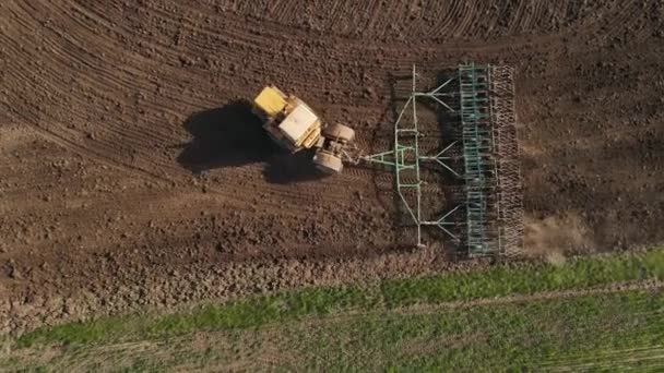 Gele trekker eggen veld grond met grote getrokken eg — Stockvideo