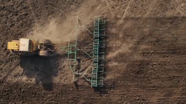 Lossa jorden med harvar tillsammans med en traktor, förbereda såbäddar för plantering vete på landsbygden, damm flyger från under hjulet, ovanifrån, skytte med drönare från en höjd — Stockvideo