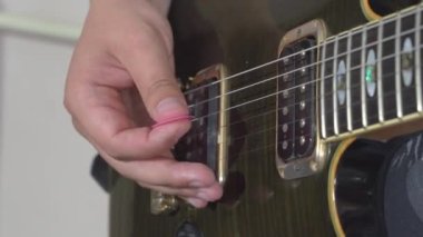 Birisi elektro gitarın tellerine vuruyor, elinde bir kazma tutuyor, yakın çekim. Müzisyen yeni melodi çalışıyor ya da öğreniyor. Hobi ve eğlence anlayışı