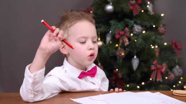 Bon garçon s'est bien comporté toute l'année, alors il écrit une lettre avec des souhaits au Père Noël et mâcher gomme ou bonbons tout en contemplant un cadeau. — Video